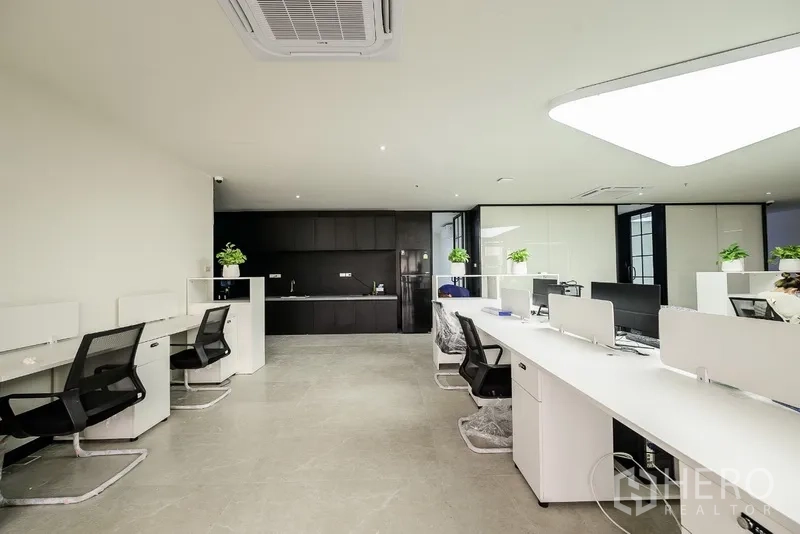 Office Space for rent or sale in Huai Khwang, Bangkok - Open-plan office with white workstations and a sleek black pantry wall in a Bangkok high-rise.