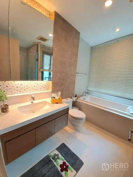 Condominium for rent or sale in Khlong Toei, Bangkok - Bright bathroom featuring a bathtub, large mirror, vanity cabinet and window blinds.