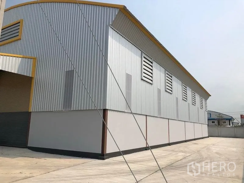 Factory for rent or sale in Bang Len, Nakhon Pathom - Side elevation of the metal-clad warehouse with louvered vents and a spacious concrete yard.