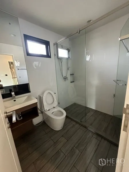 Detached House for rent or sale in Lam Luk Ka, Pathum Thani - Ensuite bathroom with glass shower enclosure, vanity and upper windows.