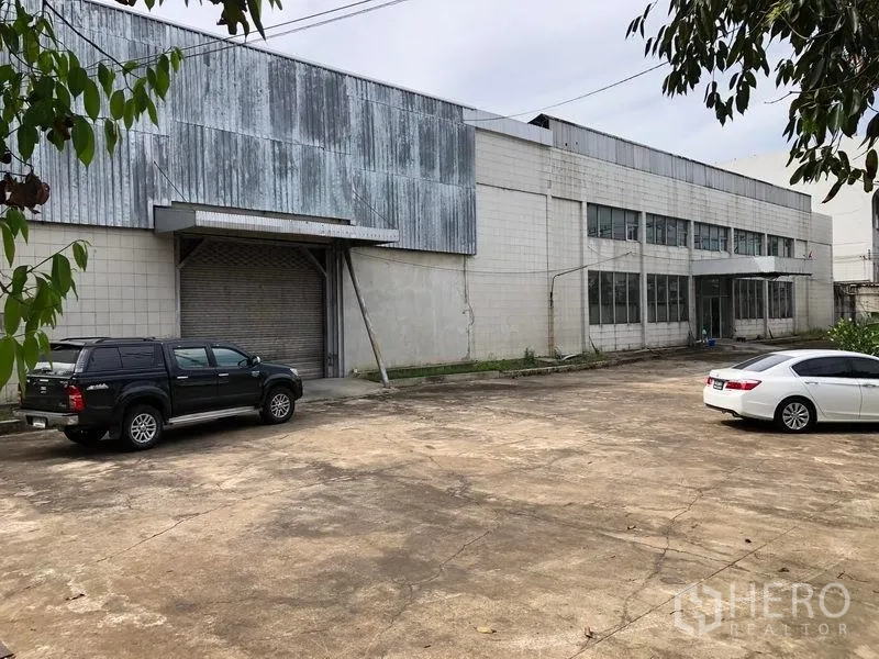 Factory for rent in Phra Pradaeng, Samut Prakan - Factory exterior with metal cladding, roller shutter loading bay and wide concrete yard for trucks.