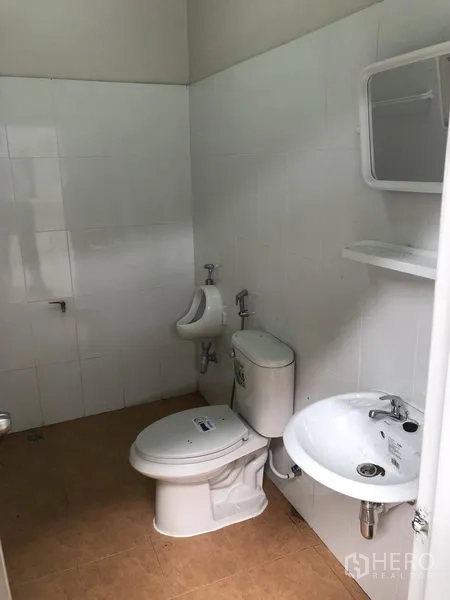 Factory for rent in Pak Kret, Nonthaburi - Clean tiled restroom with toilet, urinal and sink inside the factory.