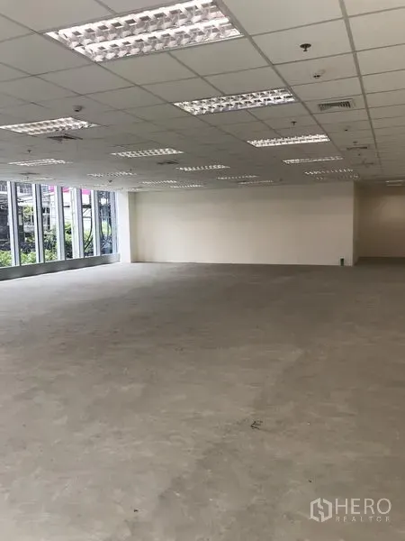 Office Space for rent in Khlong Toei, Bangkok - Spacious office interior showing a corner layout, long window wall, white walls, and suspended ceiling lighting.