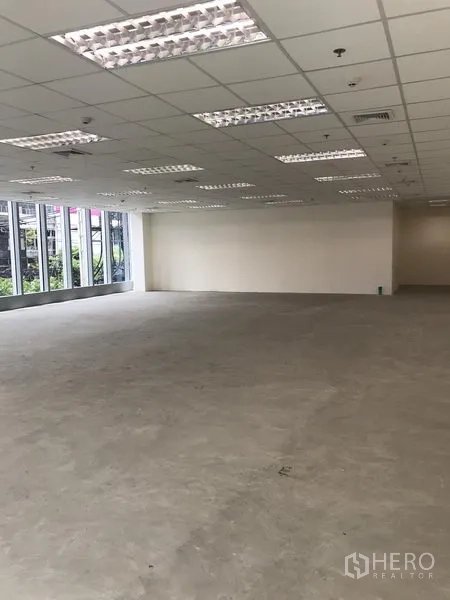 Office Space for rent in Khlong Toei, Bangkok - Spacious office interior showing a corner layout, long window wall, white walls, and suspended ceiling lighting.