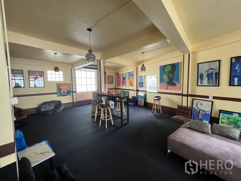 Shophouse for rent in Khlong Toei, Bangkok - Open-plan gallery-style room with carpet flooring, pendant lights and colorful wall art.