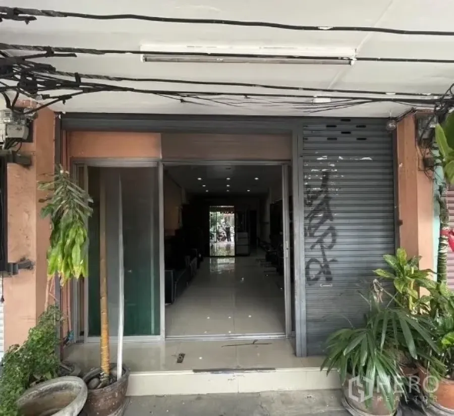Shophouse for rent in Phra Khanong, Bangkok - Shophouse entrance with partially open roller shutter and glass door.