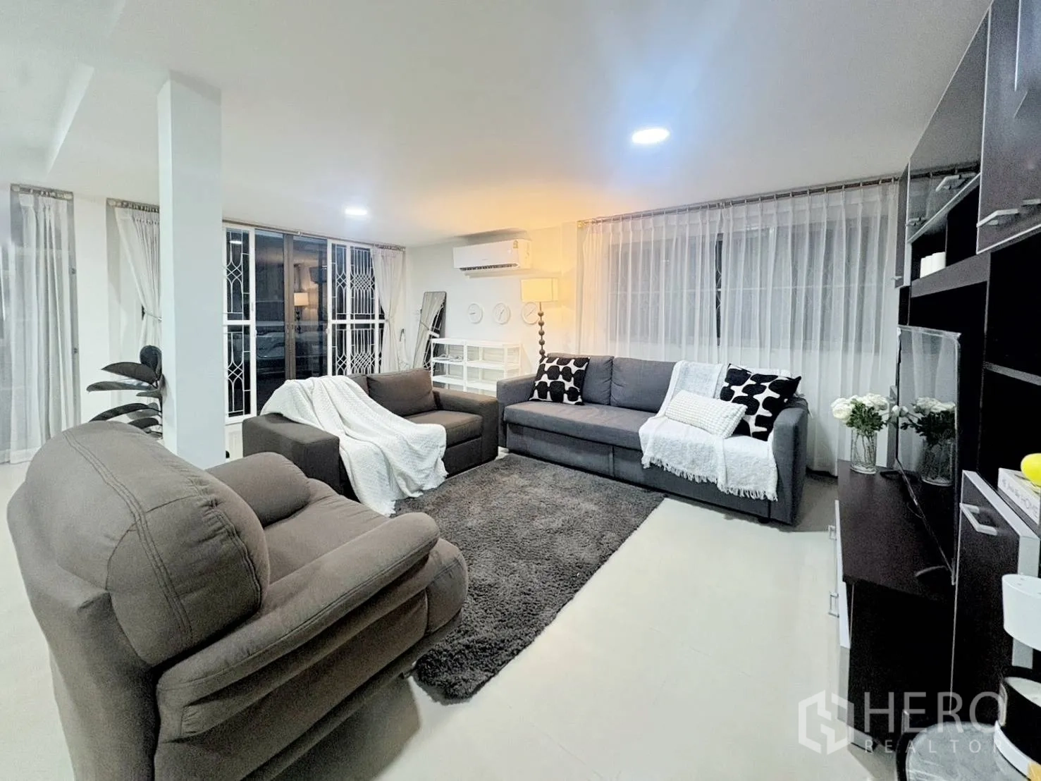 Detached House for rent in Huai Khwang, Bangkok - Airy living room with multiple sofas, rug, shelving, and wide windows.