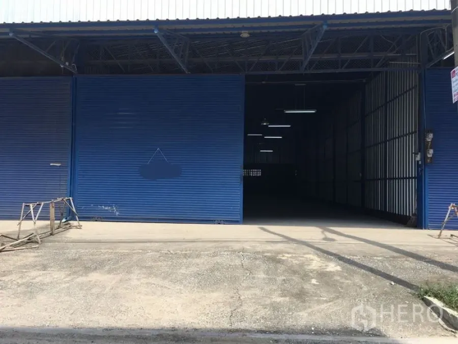 Warehouse for rent in Bang Kapi, Bangkok - Warehouse exterior showing an extra-wide blue roller shutter and a concrete loading apron suitable for pickups and small trucks.