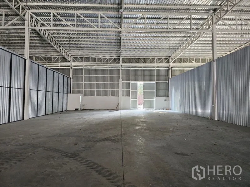 Warehouse for rent in Khlong Toei, Bangkok - Open-plan warehouse hall with high ceiling, metal walls and rear access door letting in light.