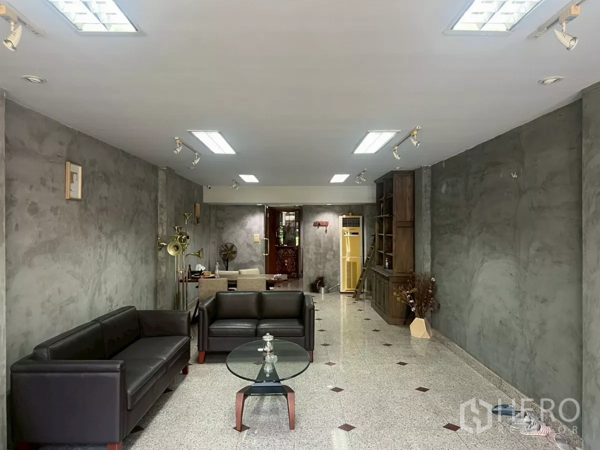 Shophouse for rent in Bang Rak, Bangkok - Ground-floor showroom with polished granite floor, grey plaster walls, sofas and track lighting.