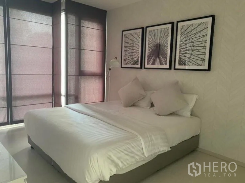 Condominium for rent in Khlong Toei, Bangkok - Bedroom with king-size bed, bedside lamp, and three framed artworks, featuring blackout blinds.