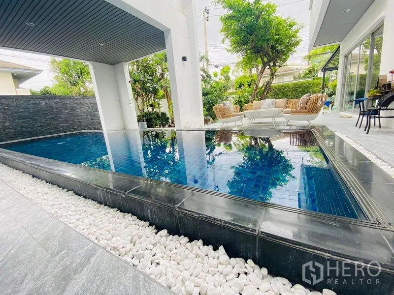 Detached House for rent in Suan Luang, Bangkok - Private swimming pool edged with white pebbles beside a covered terrace.