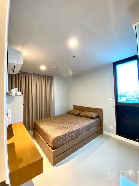 Condominium for rent in Chatuchak, Bangkok - Primary bedroom with double bed, window with curtains, and wall-mounted air conditioner.