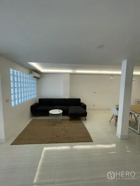 Townhouse for rent in Phra Khanong, Bangkok - Open-plan living area with black sofa, recessed lighting and a glass-block window.