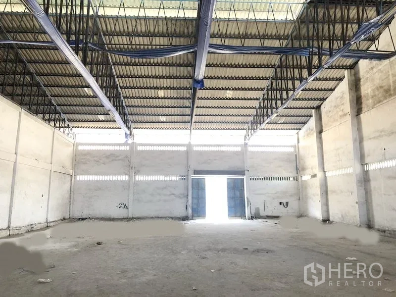Warehouse for rent in Bang Phli, Samut Prakan - Open-plan storage space with high ceiling, skylight panels and wide double metal doors for truck access.