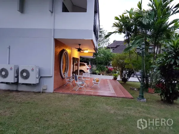 Detached House for rent in Khan Na Yao, Bangkok - Terracotta-tiled patio with outdoor seating under eaves, ceiling fan and lush landscaping beside the driveway.