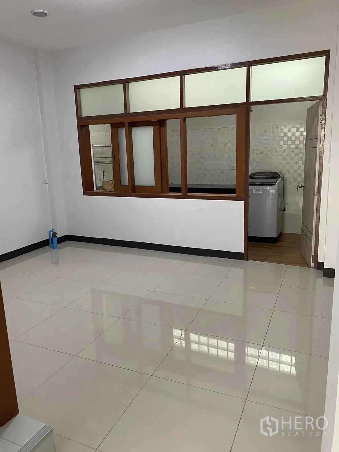 Townhouse for rent in Huai Khwang, Bangkok - Spacious living area with glossy tiles and a windowed pass-through to the kitchen.