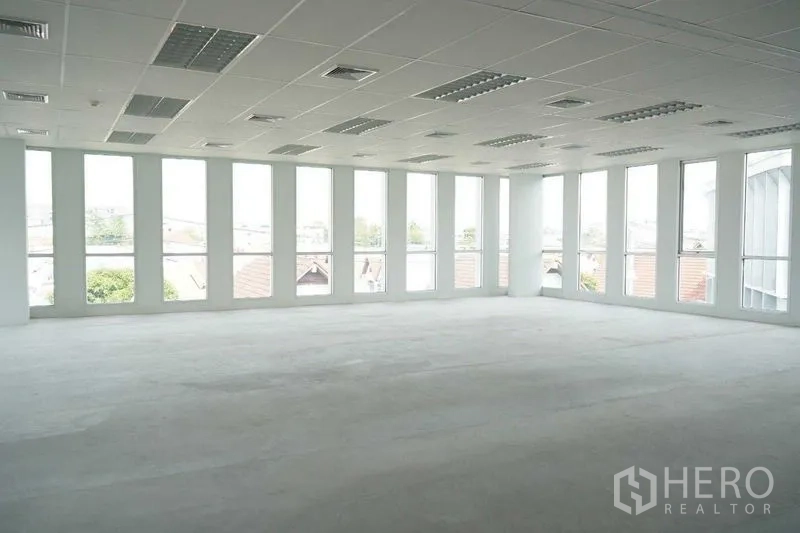 Office Space for rent in Bang Na, Bangkok - Bright open-plan office with tall windows on two sides, suspended ceiling lighting and city neighborhood views.