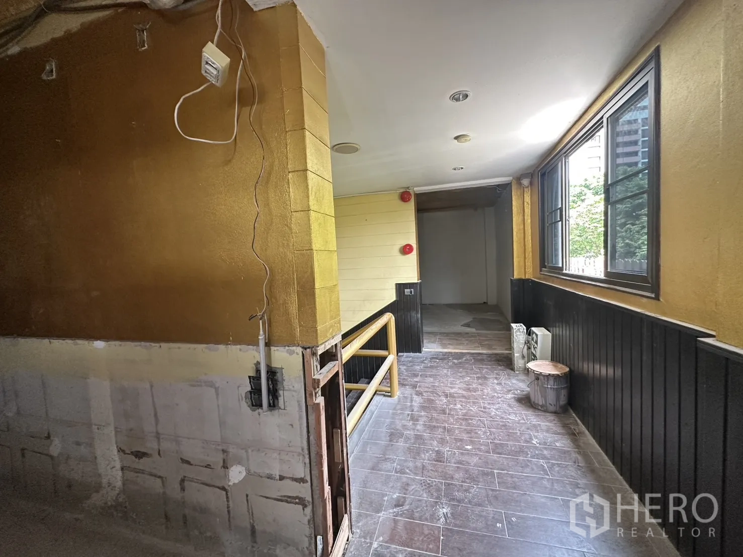 Retail Space for rent in Bang Rak, Bangkok - Corridor with gold accent wall, windows and stair rail approaching the unit entrance.