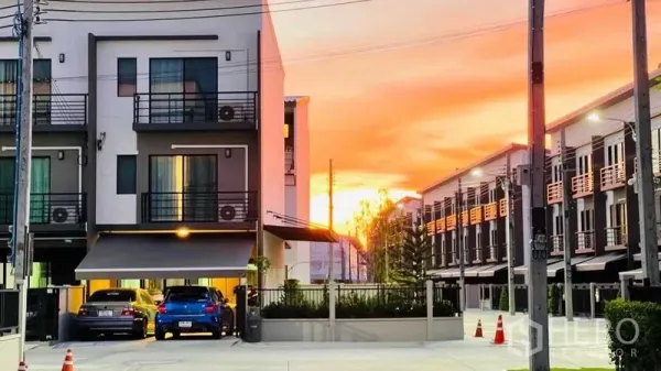Townhouse for rent or sale in Prawet, Bangkok - Modern three-storey townhouse row at sunset with covered carports and gated entrance.