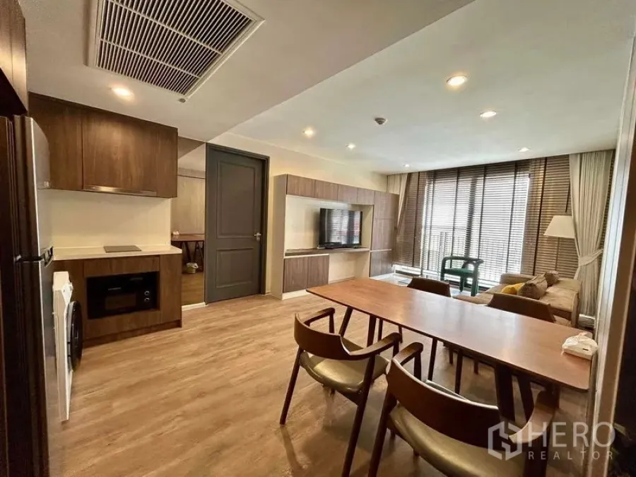 Condominium for rent - Open-plan dining and living area with long wooden table, TV console and full-height windows with blinds.