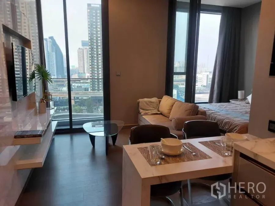 Condominium for rent in Huai Khwang, Bangkok - Living–dining area with large windows and city view beside bedroom zone.