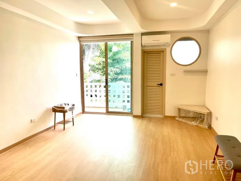 Townhouse for rent in Khlong Toei, Bangkok - Bedroom with balcony access, circular window, air-conditioning and greenery outside.
