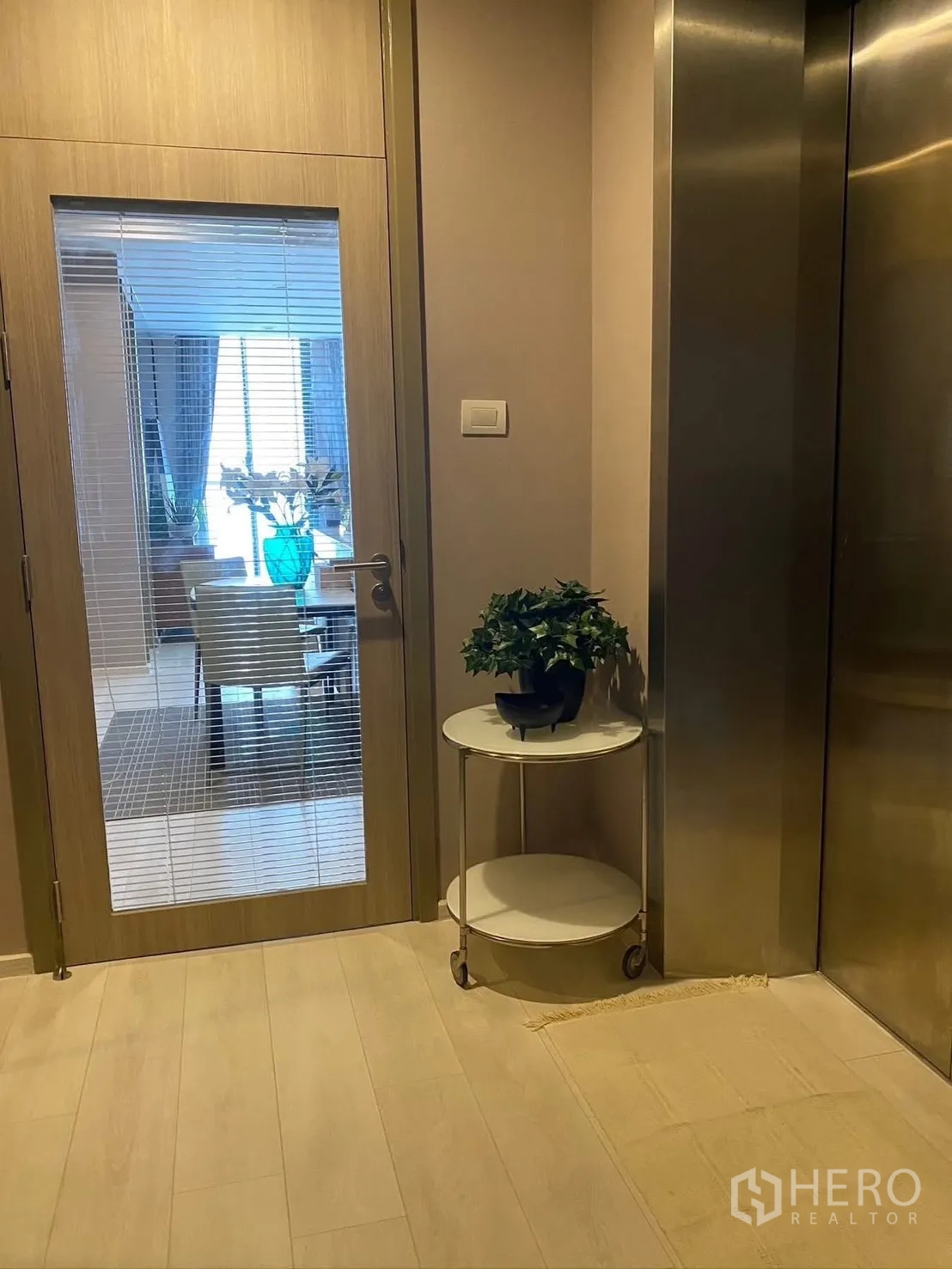 Condominium for rent in Pathum Wan, Bangkok - Private lift lobby with a glass door opening to the dining area and a small round side table with a plant.