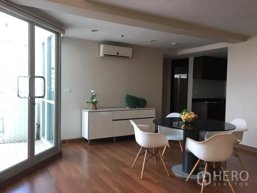Condominium for rent in Pathum Wan, Bangkok - Dining area with round table and white chairs on wood floors beside glass doors to the balcony