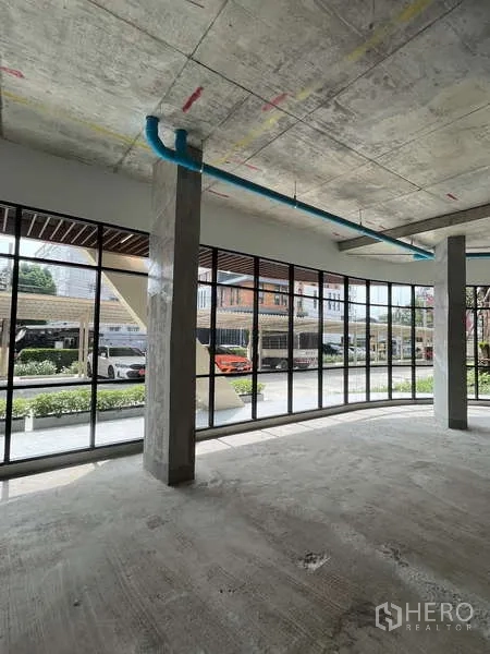 Retail Space for rent in Phra Khanong, Bangkok - Open-plan retail floor with columns, blue ceiling pipes, and parking visible outside.