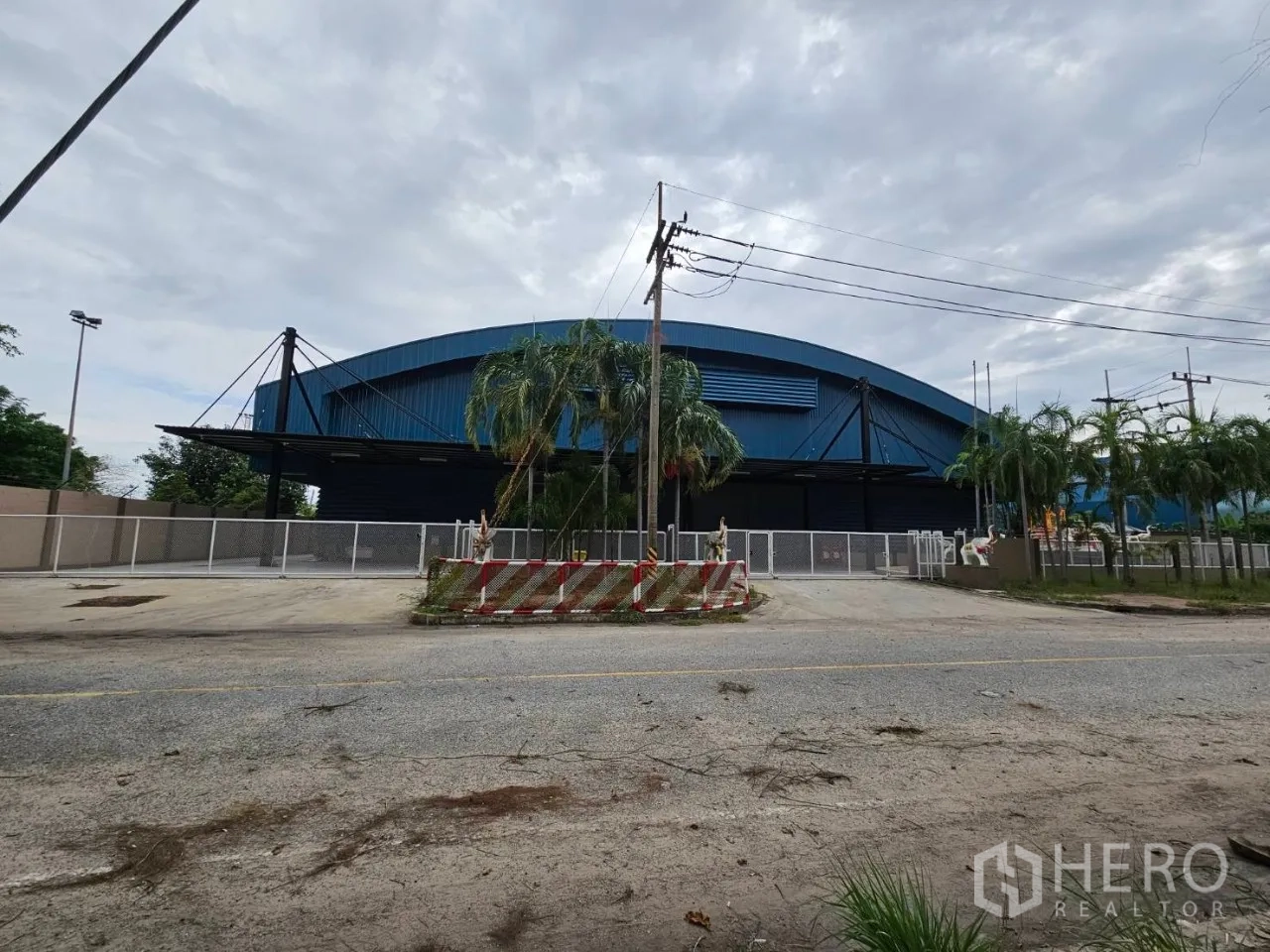 Factory for rent in Si Racha, Chon Buri - Front view of a large blue-roof factory with gated entrance and perimeter fence in Si Racha.
