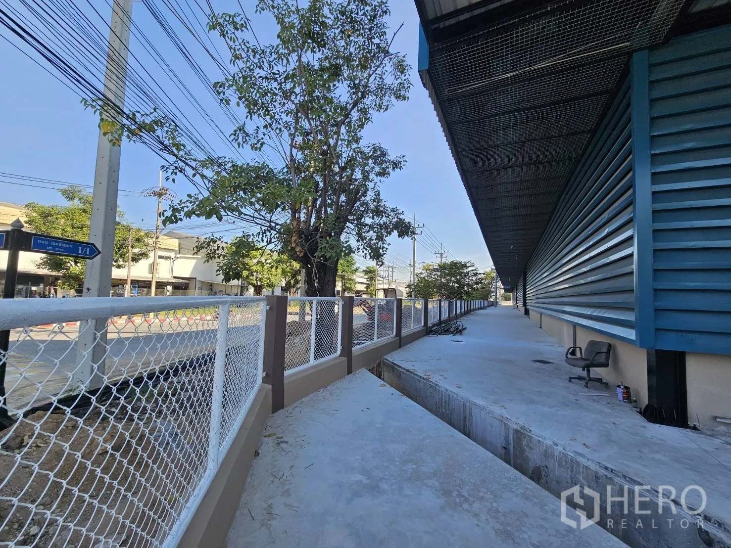Factory for rent in Chon Buri - Exterior walkway around the building with chain-link fence and a shading tree.