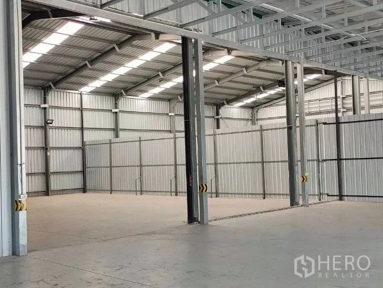 Warehouse for rent in Pak Kret, Nonthaburi - Spacious clear-span warehouse bay with skylight roof panels, concrete floor, and steel columns.