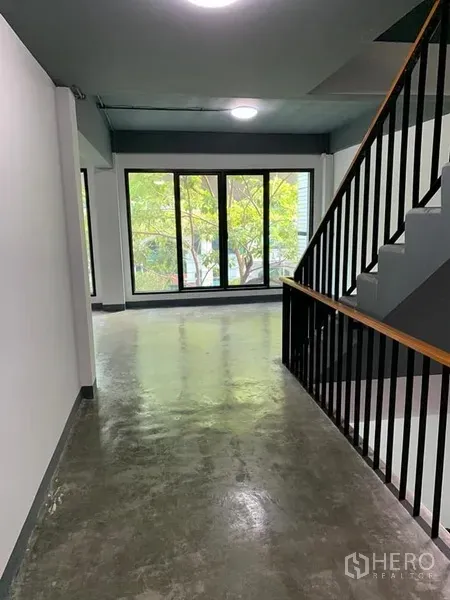 Shophouse for rent in Khlong Toei, Bangkok - Corridor with black metal staircase and floor-to-ceiling windows overlooking greenery.