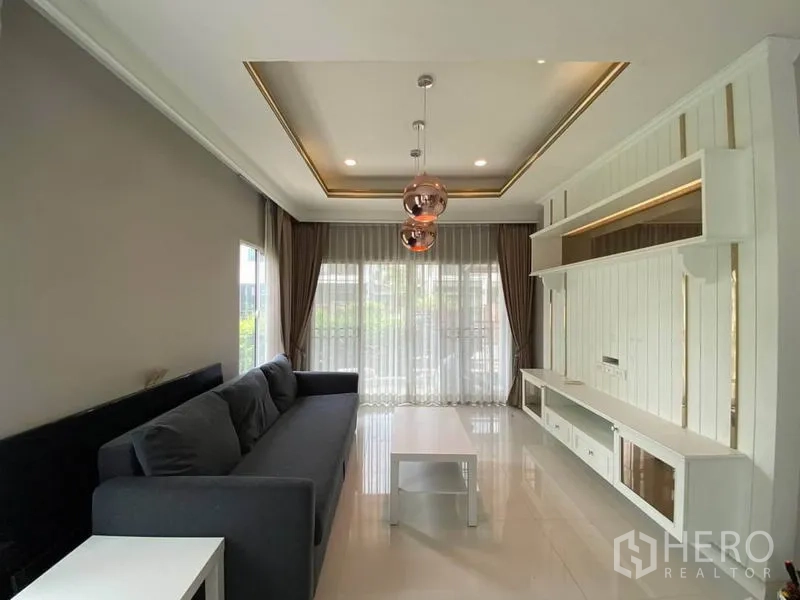 Detached House for rent in Suan Luang, Bangkok - Modern living room with floor-to-ceiling sheer curtains, built-in TV wall and stylish pendant lights.