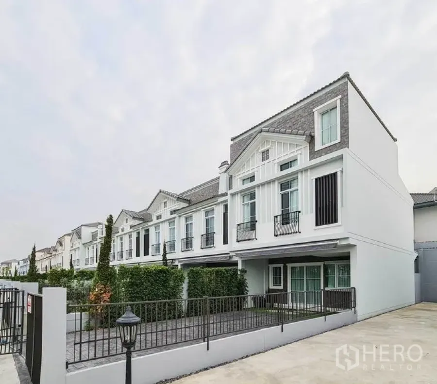 Townhouse for rent in Prawet, Bangkok - Modern townhouse row with gabled roof, large windows, gated driveway and front yard.
