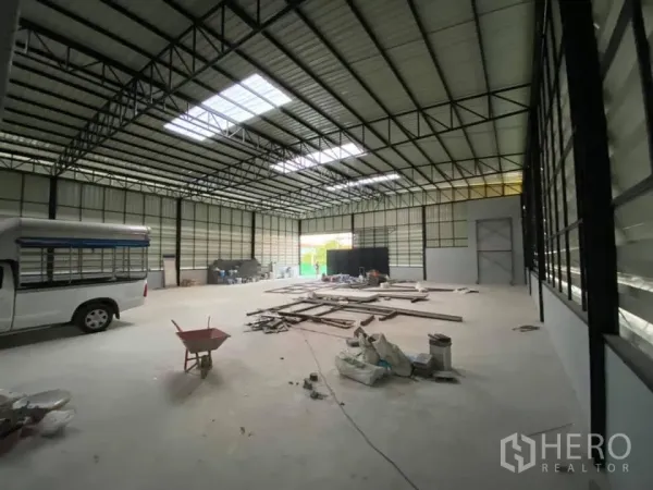 Warehouse for rent in Saphan Sung, Bangkok - Spacious warehouse interior with high steel trusses, skylights and a concrete floor, with a vehicle and materials inside.