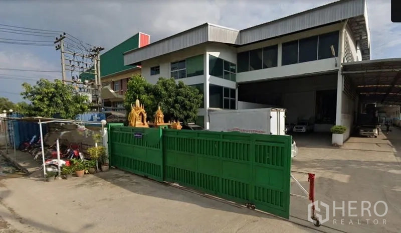 Factory for sale in Khlong Luang, Pathum Thani - Two-storey factory exterior in Khlong Luang with a wide covered loading bay and green sliding gate.