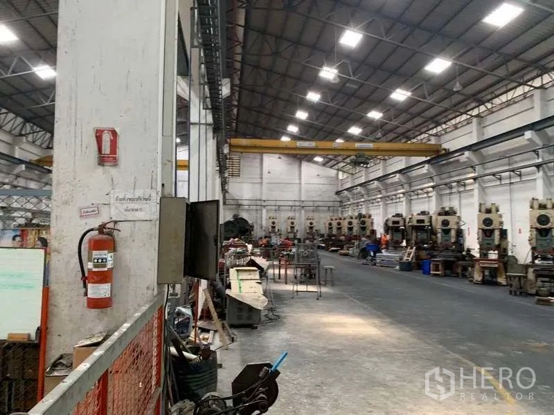 Factory for rent in Samut Prakan - Long factory aisle showing machinery rows, safety signage and crane rails above.