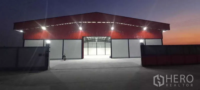 Warehouse for rent or sale in Khlong Luang, Pathum Thani - Front view with main doors open revealing the illuminated clear-span interior of the warehouse.