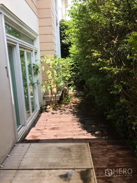 Townhouse for sale in Huai Khwang, Bangkok - Shaded side garden walkway with sliding glass doors and mature plants.