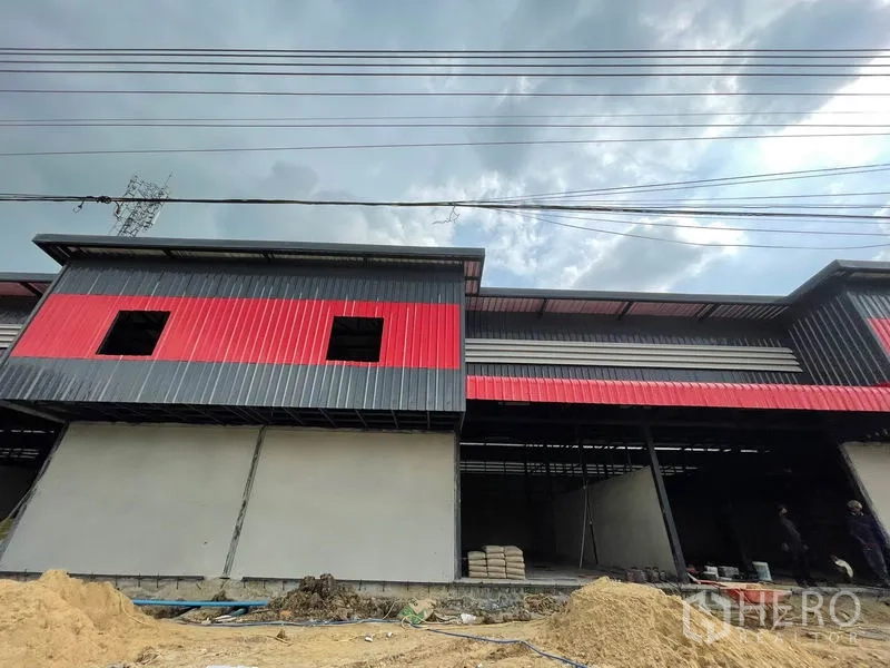 Warehouse for rent in Pathum Thani - Low-angle exterior highlighting roof overhang, overhead power lines and red panels.
