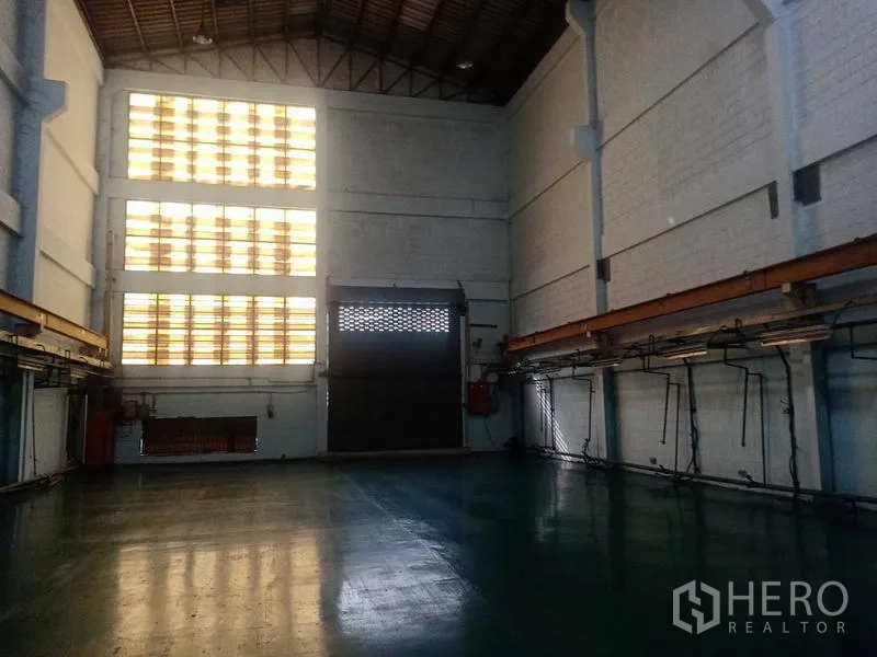 Factory for sale in Khlong Luang, Pathum Thani - Loading bay with tall roller shutter door and ventilated glass block wall.