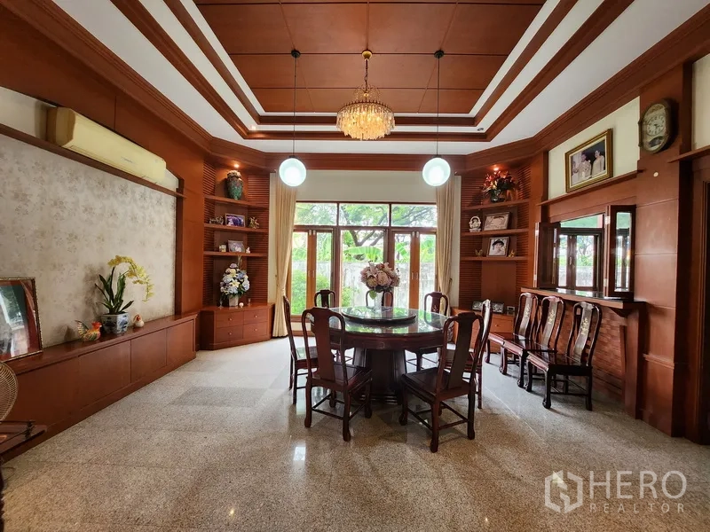 Detached House for rent in Prawet, Bangkok - Formal dining room with coffered ceiling, built‑in wood shelves and round table facing garden windows.