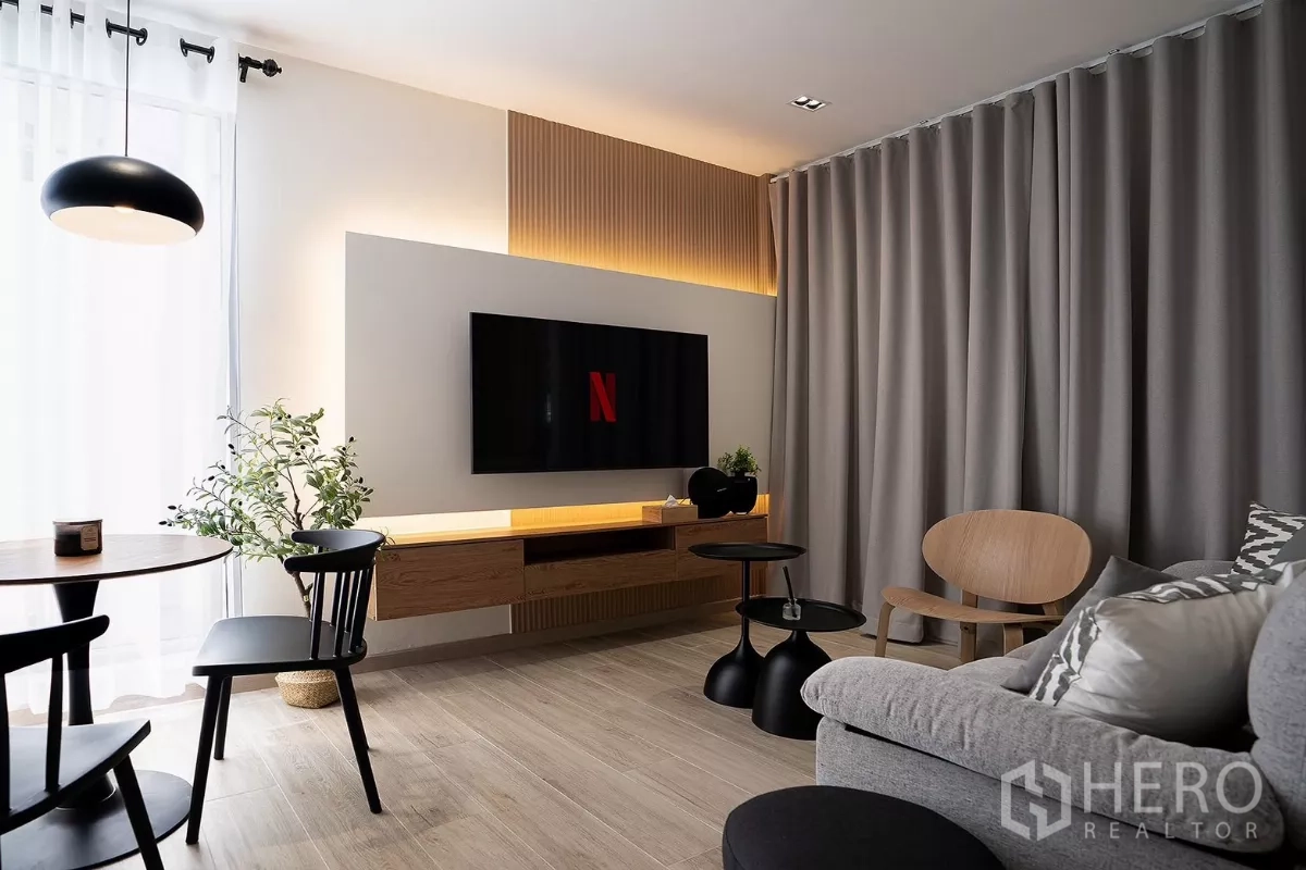 Detached House for rent in Huai Khwang, Bangkok - Modern living room with wall-mounted TV, grey sofa and a dining nook.