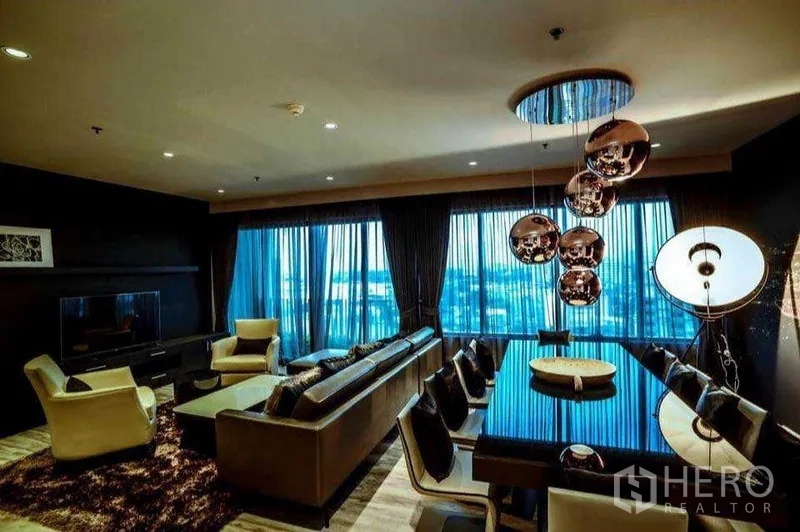 Condominium for rent or sale in Khlong Toei, Bangkok - Living and dining room with sectional sofa, TV console and sculptural pendant lights.