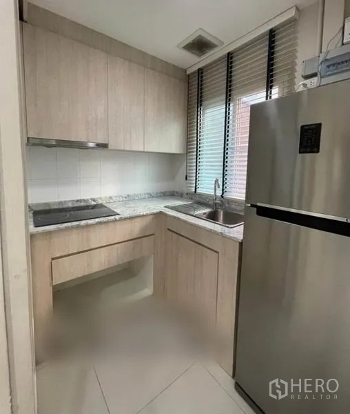 Townhouse for sale in Suan Luang, Bangkok - Compact U-shaped kitchen with light wood cabinets, marble-look countertop, sink under window and stainless fridge.
