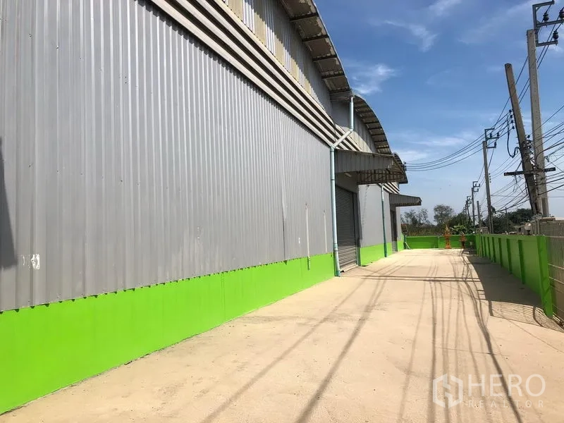 Warehouse for rent in Lat Krabang, Bangkok - Exterior of corrugated metal warehouse with loading bays and a wide truck driveway in the Romklao area.