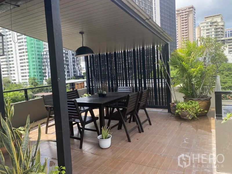Condominium for rent in Khlong Toei, Bangkok - Covered terrace with outdoor dining set and lush greenery overlooking the city.