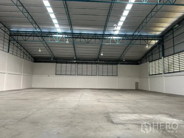 Factory for rent in Si Racha, Chon Buri - Clear-span warehouse floor with high-bay lighting and louvered side walls for airflow.